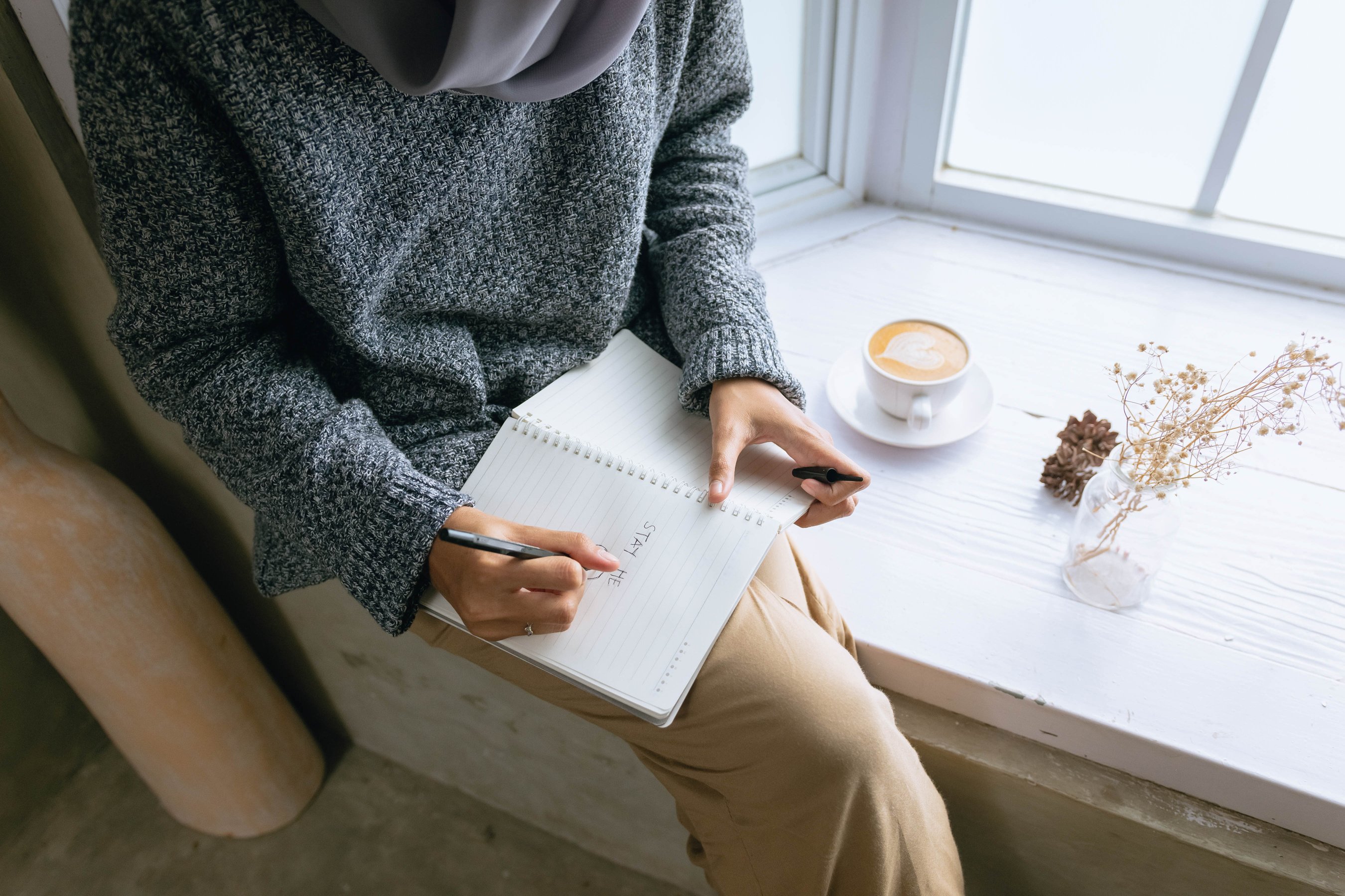 Person Writing on a Notebook by the Windowsill